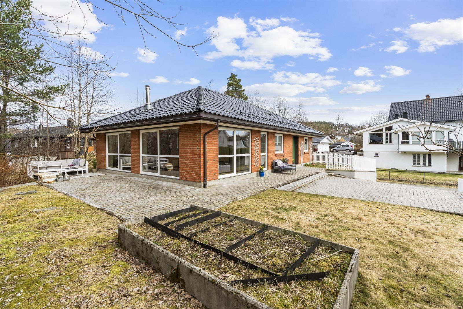 Tomten er pent opparbeidet med gressplen, blomsterbed, variert beplantning og et klassisk hvitmalt stakittgjerde. Galleribilde