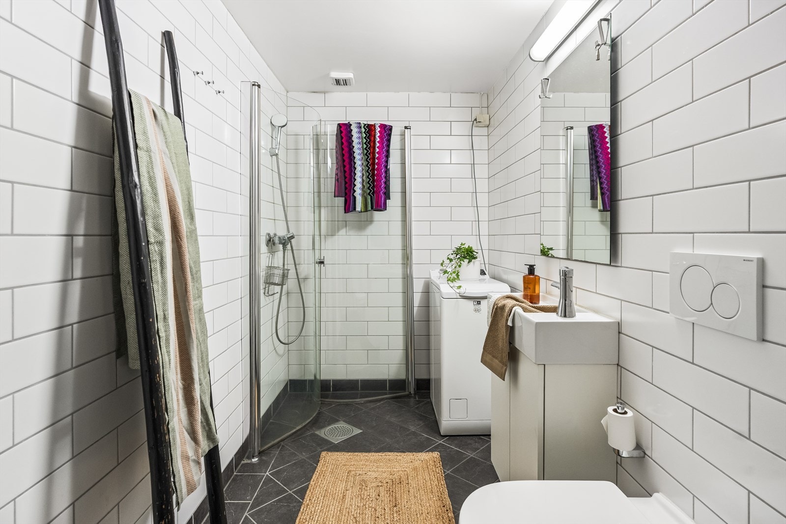 Badet har hvite veggfliser og mørke gulvfliser med varme. Galleribilde