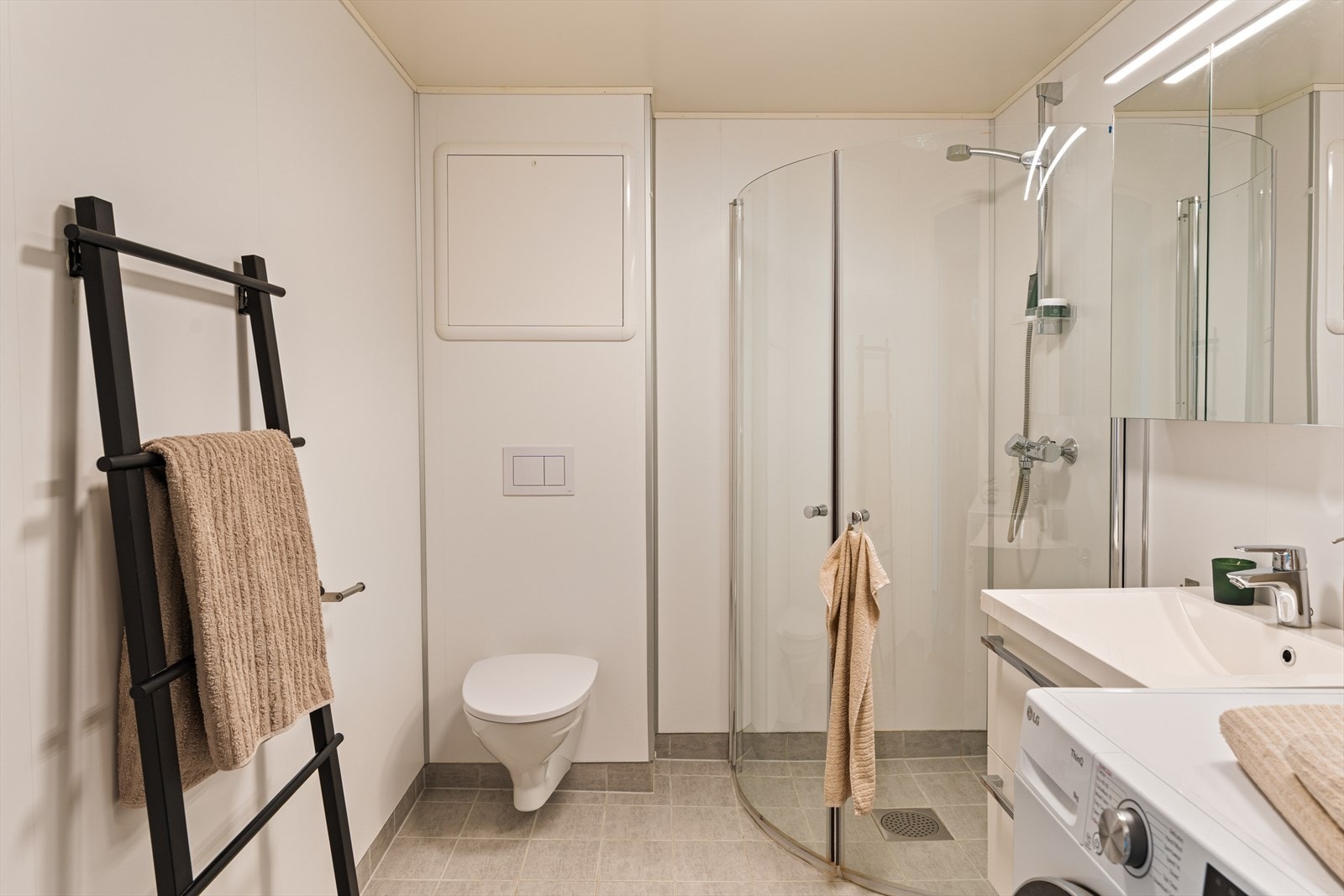 Badet er moderne og er utstyrt med vegghengt toalett, helstøpt servant med underskuffer, dusjdører i klart glass og opplegg for vaskemaskin Galleribilde
