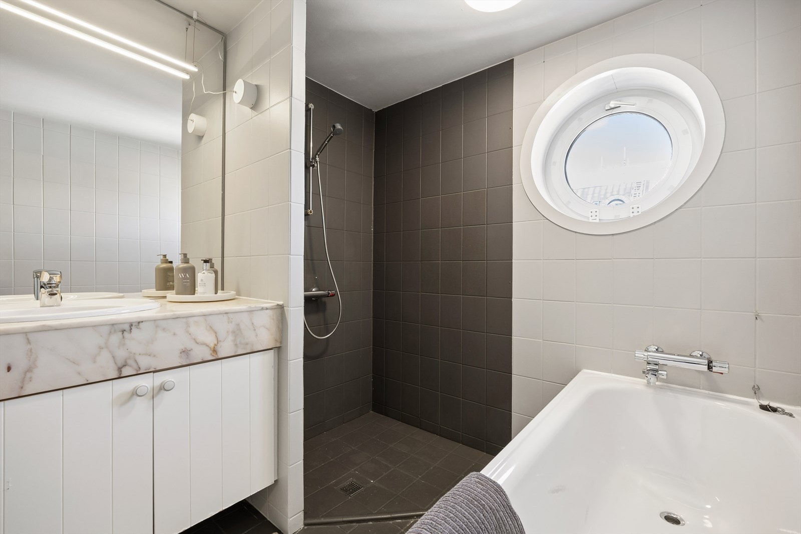 Badet har flislagte overflater og et karakteristisk rundt vindu i plast som gir et maritimt preg. Galleribilde