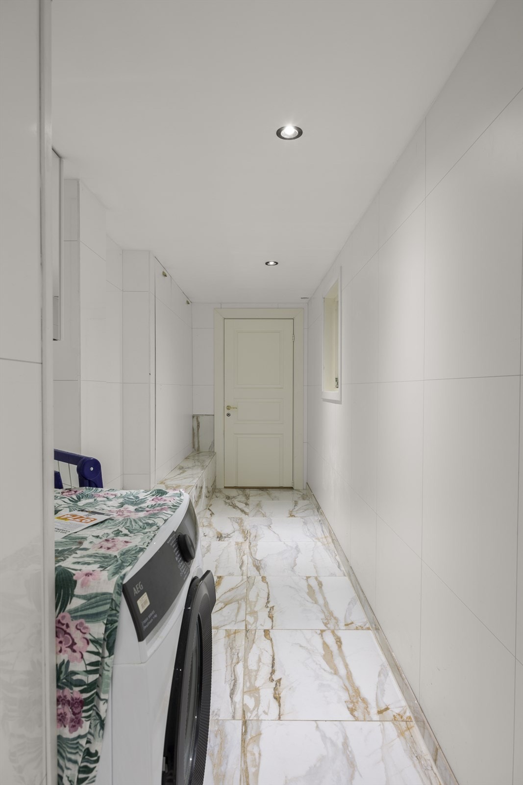 Veggene har baderomsplater. Taket er malt med downlights. Gulvet er flislagt. Rommet har vannbåren gulvvarme. Vaskerommet er praktisk innredet med servant, servantarmatur og benkeplate. Opplegg for vaskemaskin. Det er naturlig ventilering. Galleribilde
