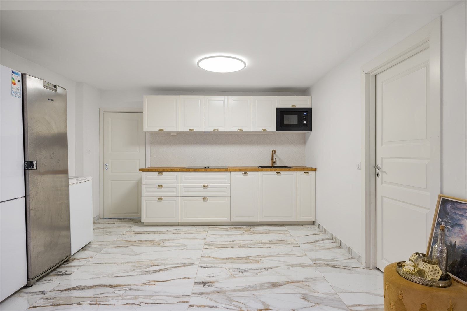 Kjøkkenet i kjeller har innredning med profilerte fronter. Benkeplaten er av heltre. Det er kjøl/fryseskap, oppvaskmaskin, induksjonstopp, micro og vannstoppsystem. Det er kjøkkenventilator med kullfilter. Galleribilde