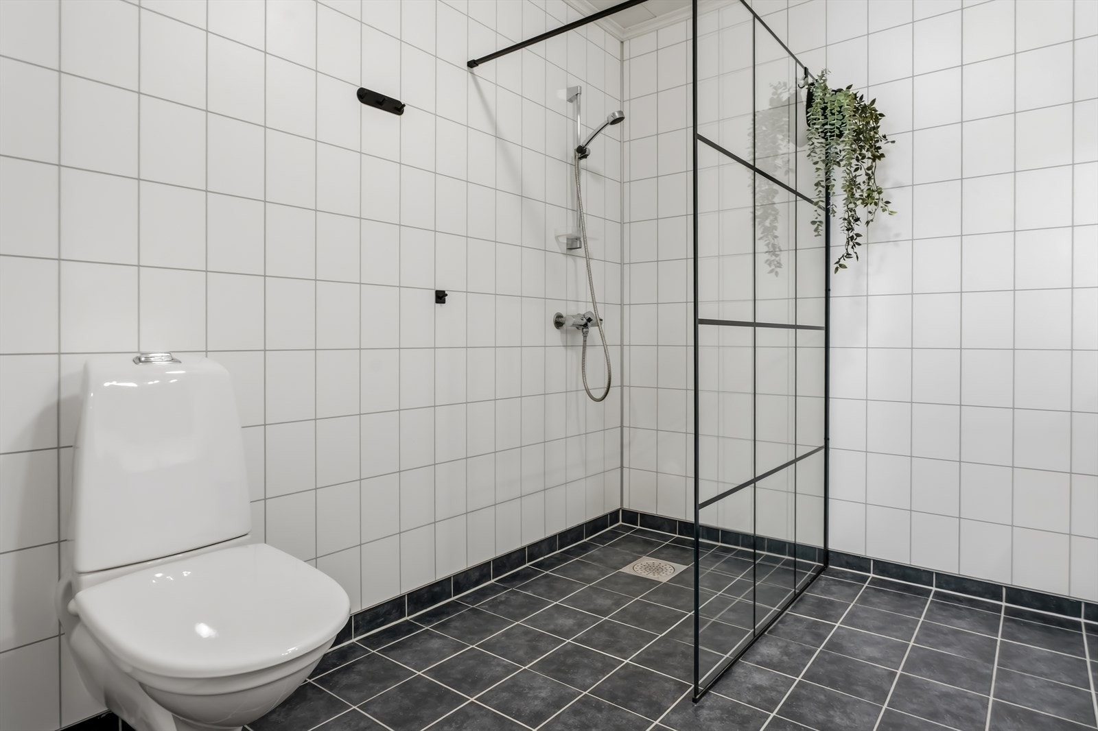 Vegghengt toalett og en dusjnisje med glassdør. Rommet ventileres med avtrekk fra det balanserte ventilasjonsanlegget. Galleribilde