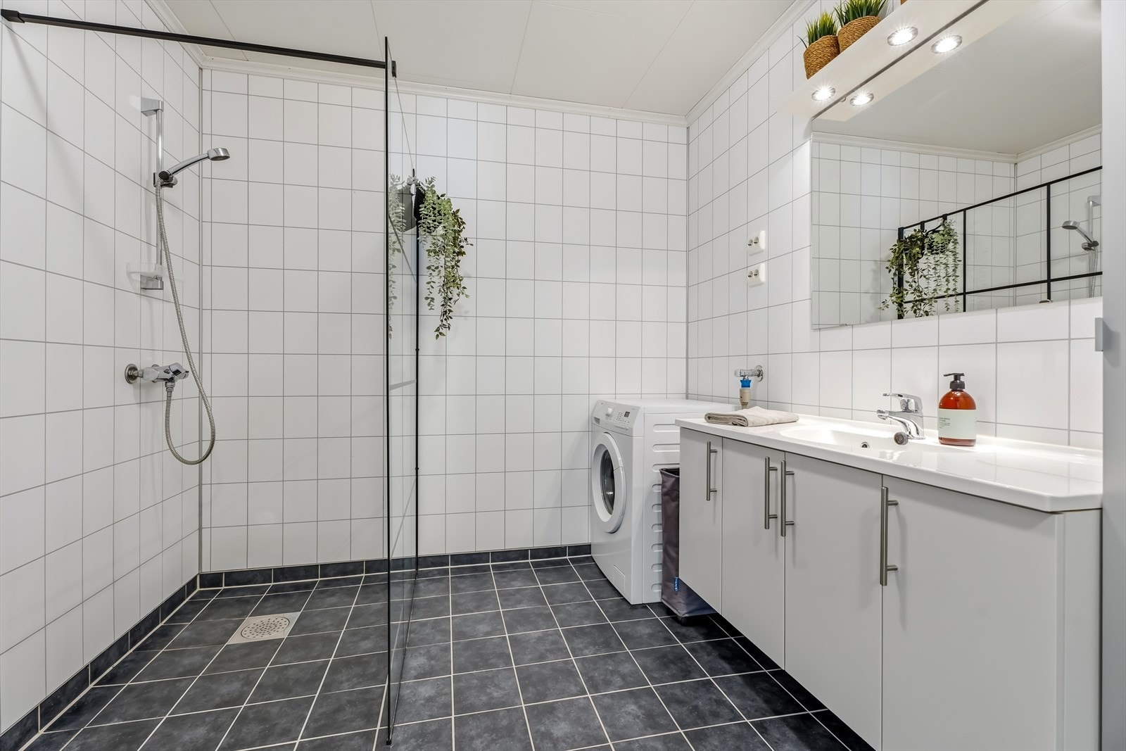 Badet har tidløse flislagte overflater og har elektriske varmekabler i gulvet. Innredet med servantskap med overliggende servant, vegghengt speil med belysning, Opplegg for vaskemaskin Galleribilde