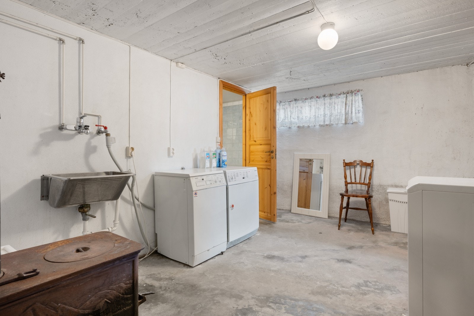 Romslig vaskerom i kjeller med støpt betonggulv, utslagsvask og opplegg for vaskemaskin. Galleribilde