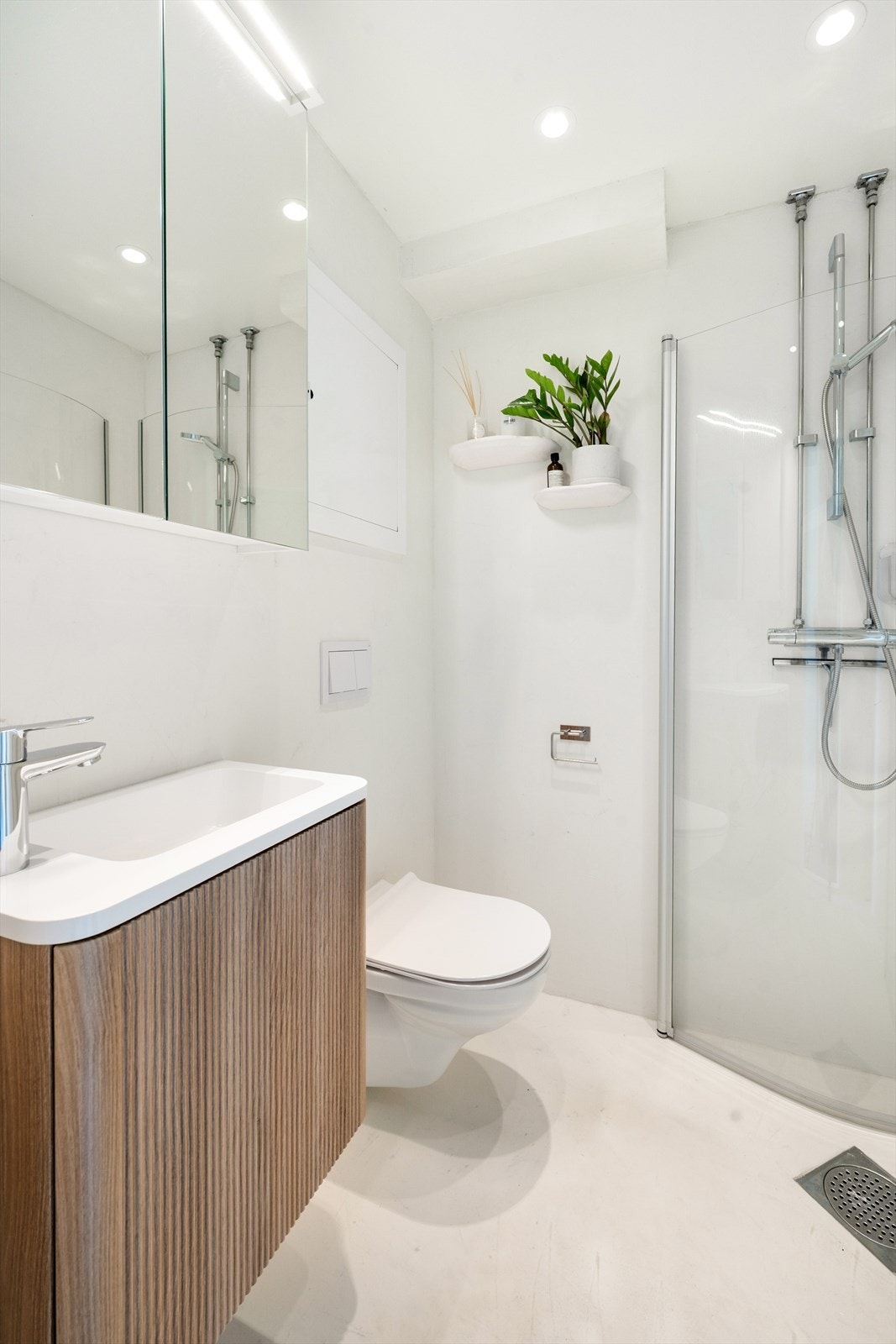 Badet er innredet med nedfelt servant, speilskap, veggmontert toalett og dusjvegger/hjørne. Galleribilde