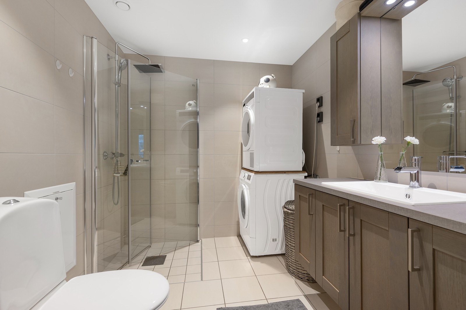 Badet fremstår som delikat og funksjonelt, med helflisede overflater i lyse og tidsriktige toner. Det er gulvvarme og downlights i himling som gir god komfort og belysning. Galleribilde