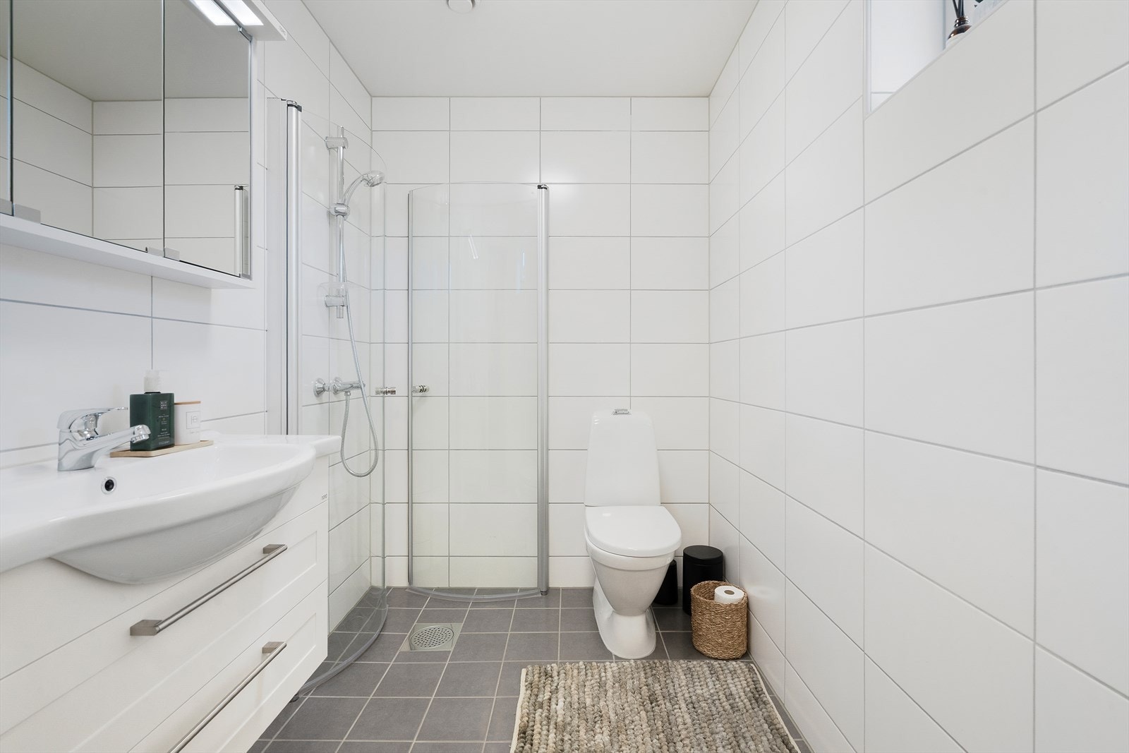 Pent bad i 1.etasje i tilknytning til entrèeen med hvit baderomsinnredning, speilskap, toalett og dusjhjørne med innfellbare dusjdører. Galleribilde