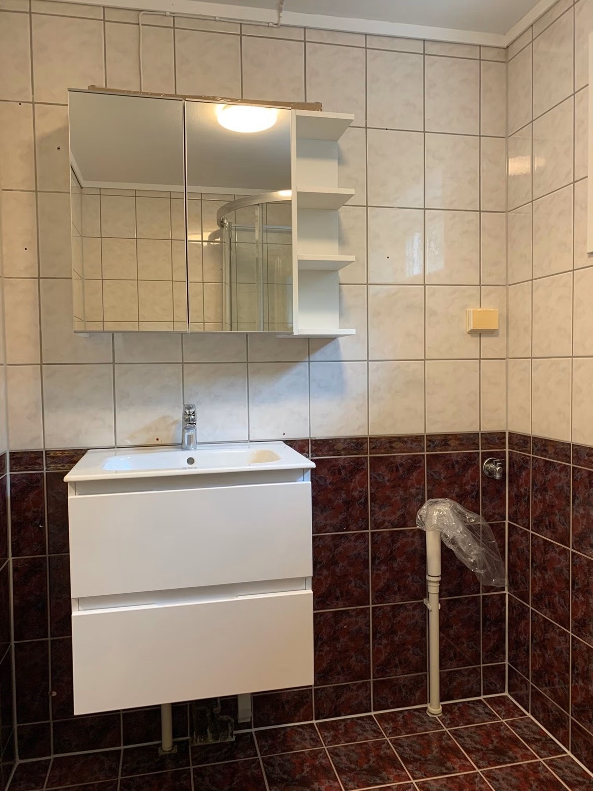 Baderom med fliser på gulv og vegger, og malt strie i tak. Rommet er utstyrt med dusjkabinett, klosett, servant med skuffer, speilskap og opplegg for vaskemaskin. Galleribilde