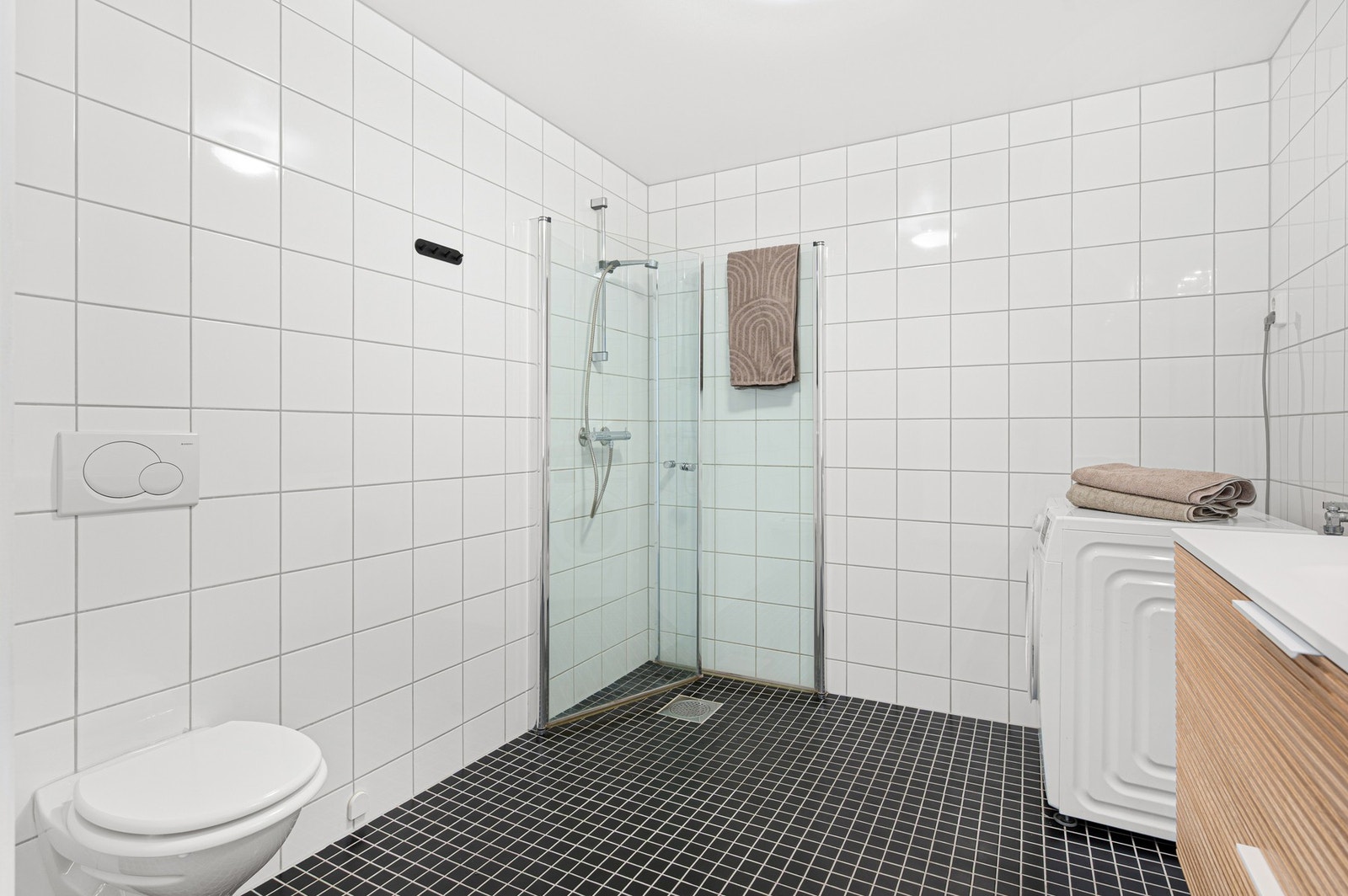 Badet er innredet med servantinnredning, speil med overlys, vegghengt toalett og dusjhjørne. Galleribilde