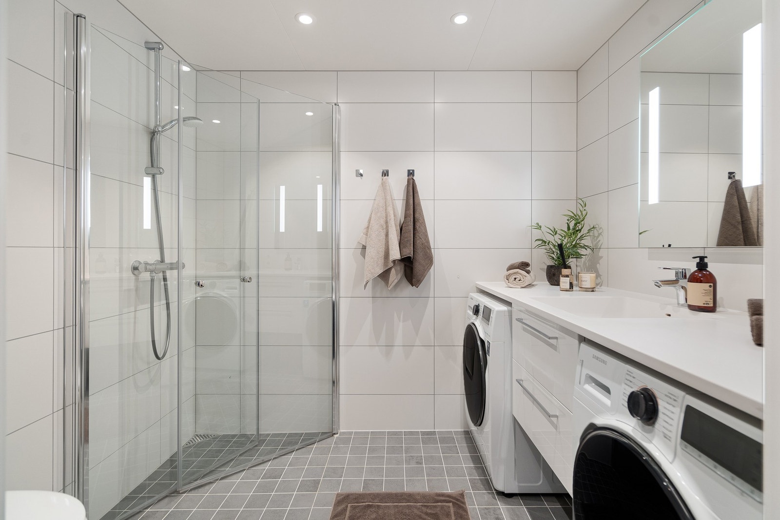 Delikat og moderne baderom med stilrene flislagte overflater og gjennomført design. Badet byr på en romslig dusjløsning med glassvegger, praktisk innredning med god oppbevaringsplass og egen løsning for vaskemaskin og tørketrommel. Galleribilde