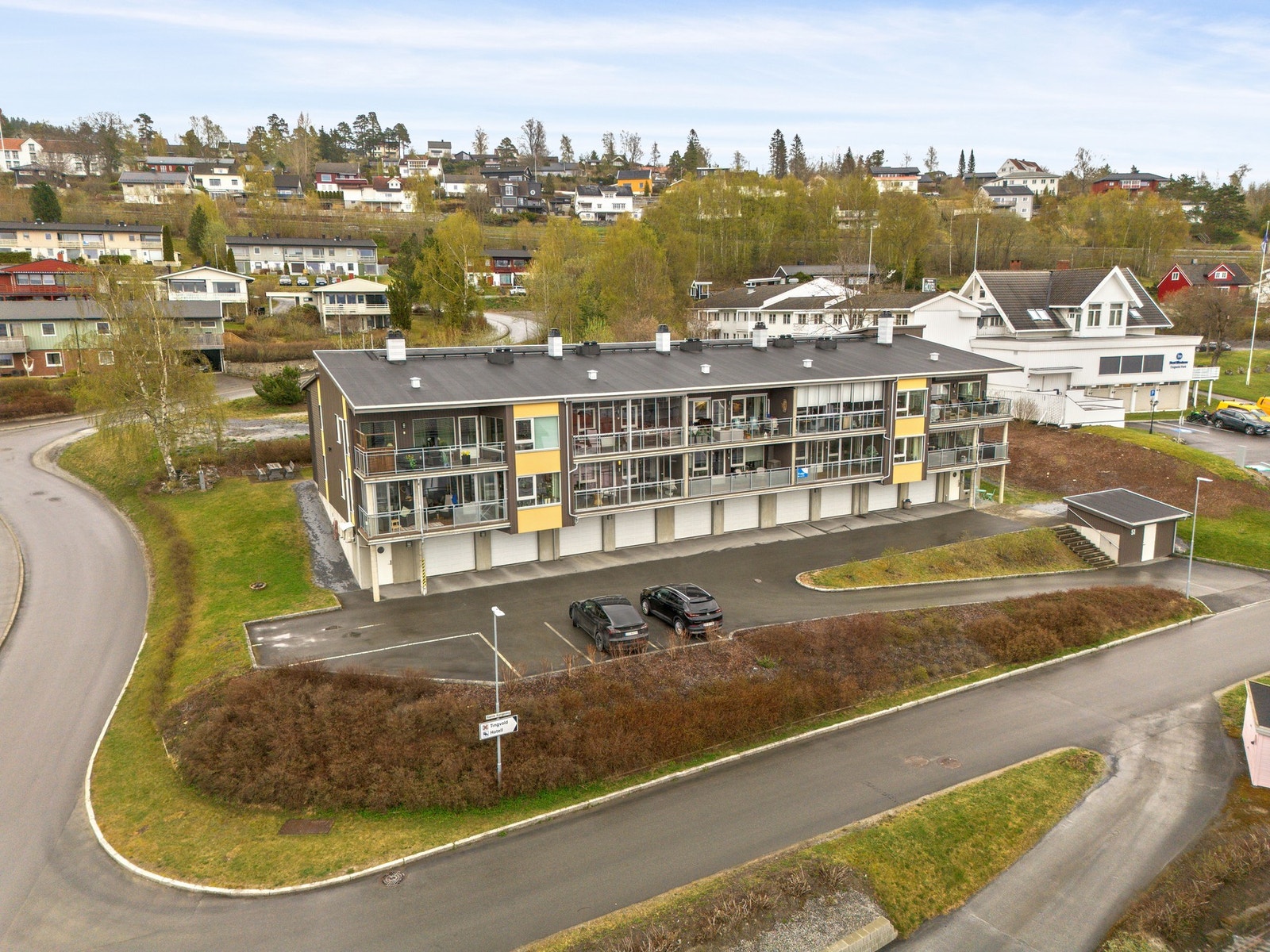 Asfaltert uteområde. Fellesarealet er pent opparbeidet med plen og busker. Galleribilde
