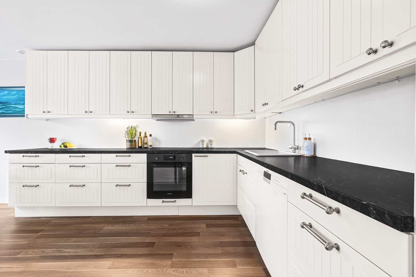 Kjøkkeninnredningen fra IKEA (2012) har profilerte, folierte fronter og laminat benkeplate med nedfelt keramisk kum, samt belysning under overskap som gir et praktisk arbeidslys. Galleribilde