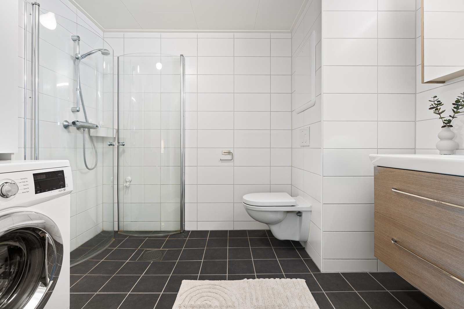 Delikat flislagt baderom med dusjhjørne, vegghengt wc og moderne innredning.