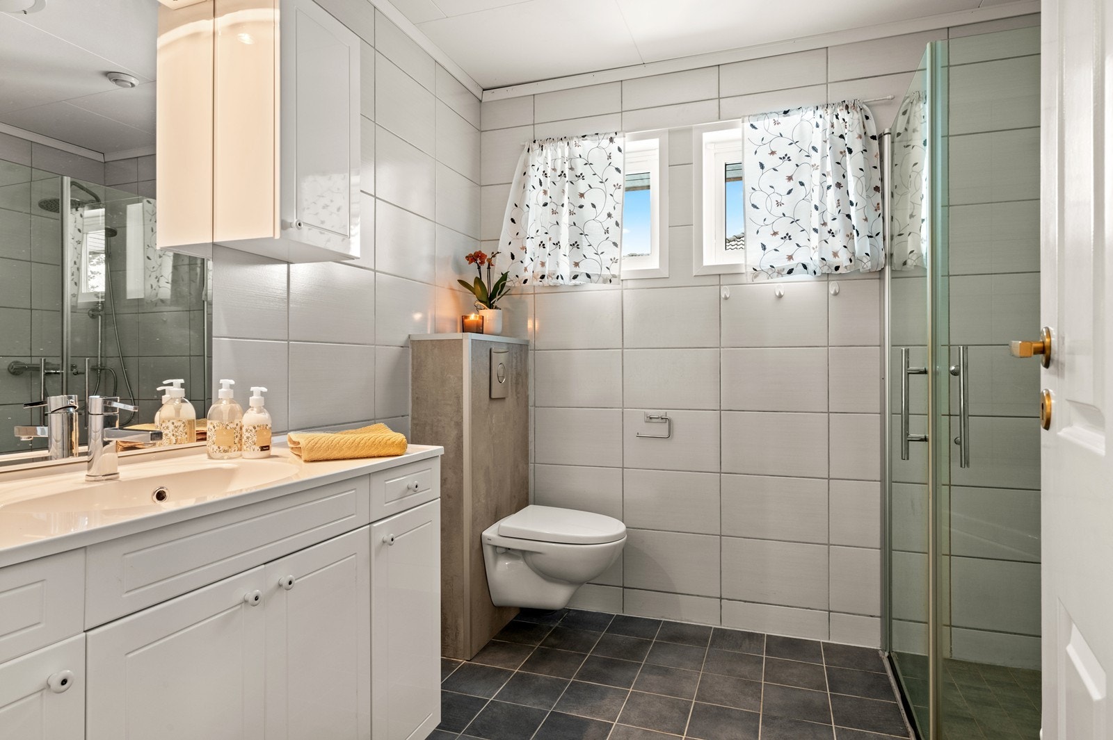 Badet i første etasje ble oppgradert i 2012 og er helfliset, og har elektrisk gulvvarme. Det er utstyrt med baderomsinnredning med heldekkende servant, og speil over servanten med overskap. I tillegg er det vegghengt wc. Galleribilde
