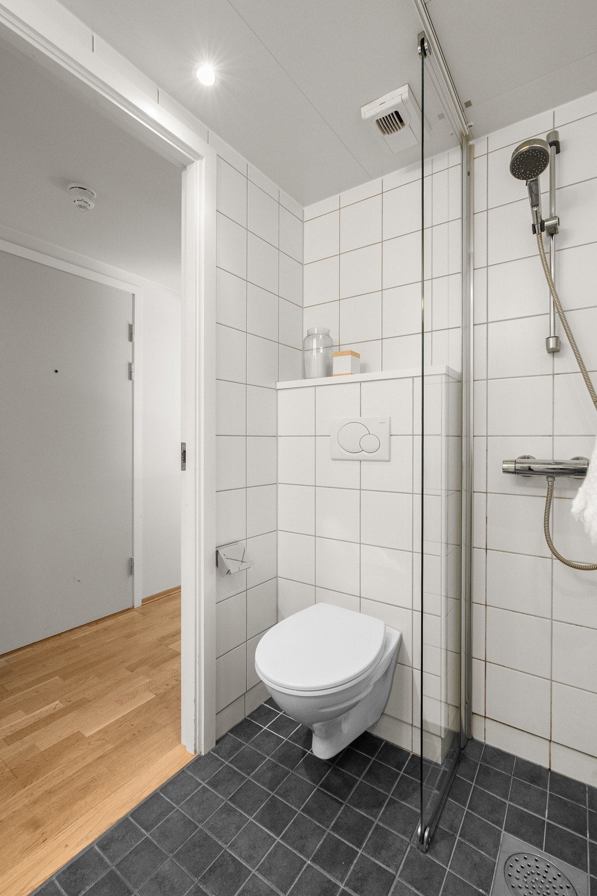 Baderommet har mørke fliser på gulv, deilig gulvvarme, hvite fliser på veggene, downlights i himlingen og mekanisk avtrekk med ventil i himling. Galleribilde