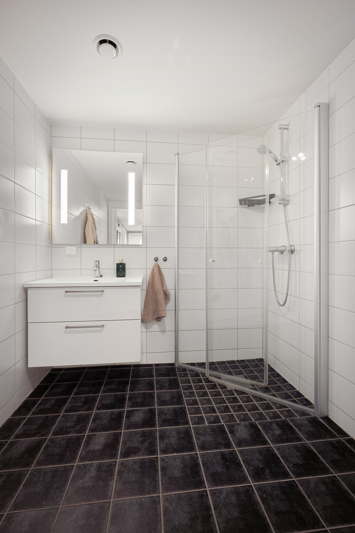 Badet har en stilren innredning med vegghengt toalett, servant med underskap og speil med belysning, samt en praktisk dusjsone med foldbare dusjdører som gir god plassutnyttelse. Galleribilde