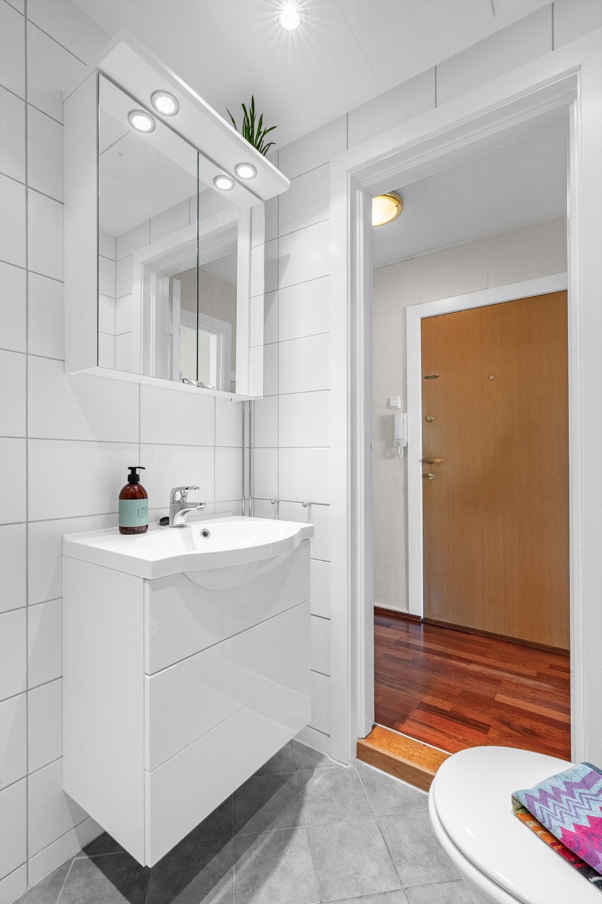 Moderne baderomsinnredning, med heldekkende servant i skuffeinnredning, og med tilhørende speilskap på vegg i samme stil. Videre er baderommet utstyrt med veggmontert klosett, samt opplegg for vaskemaskin. Galleribilde