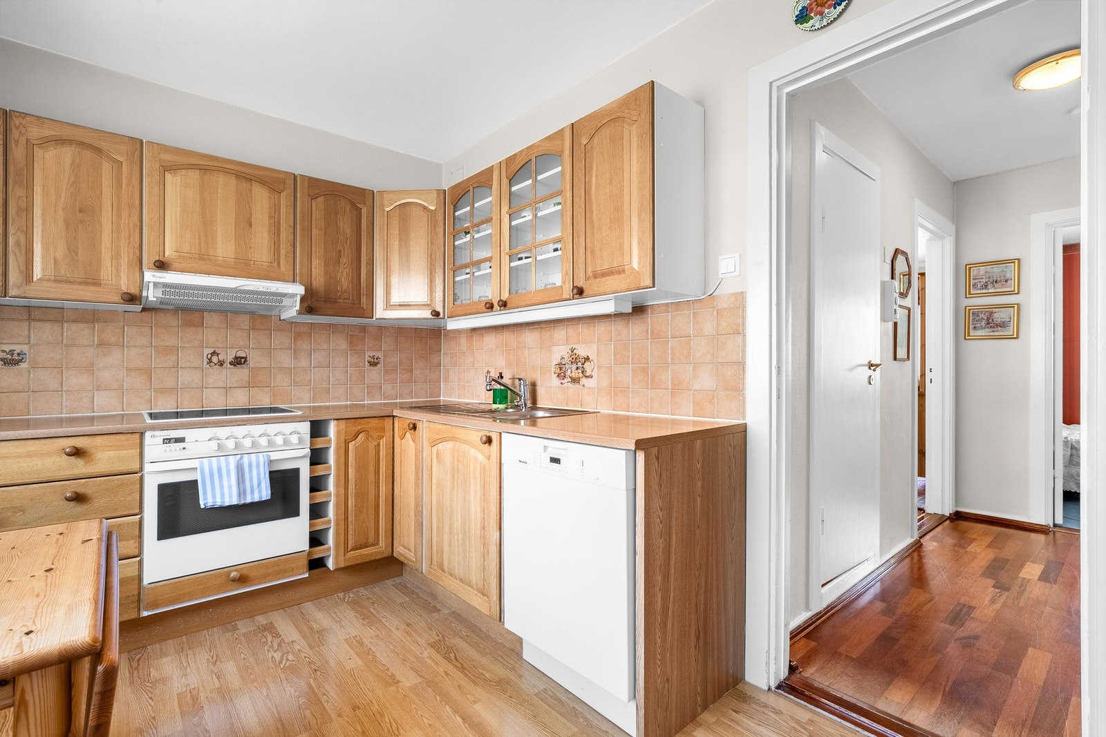 Kjøkkeninnredning med profilerte fronter, og noen vitrinefronter. Benkeplaten er av laminat, med nedfelt kum i rustfritt stål. Det er lagt fliser på vegg over benk. Galleribilde