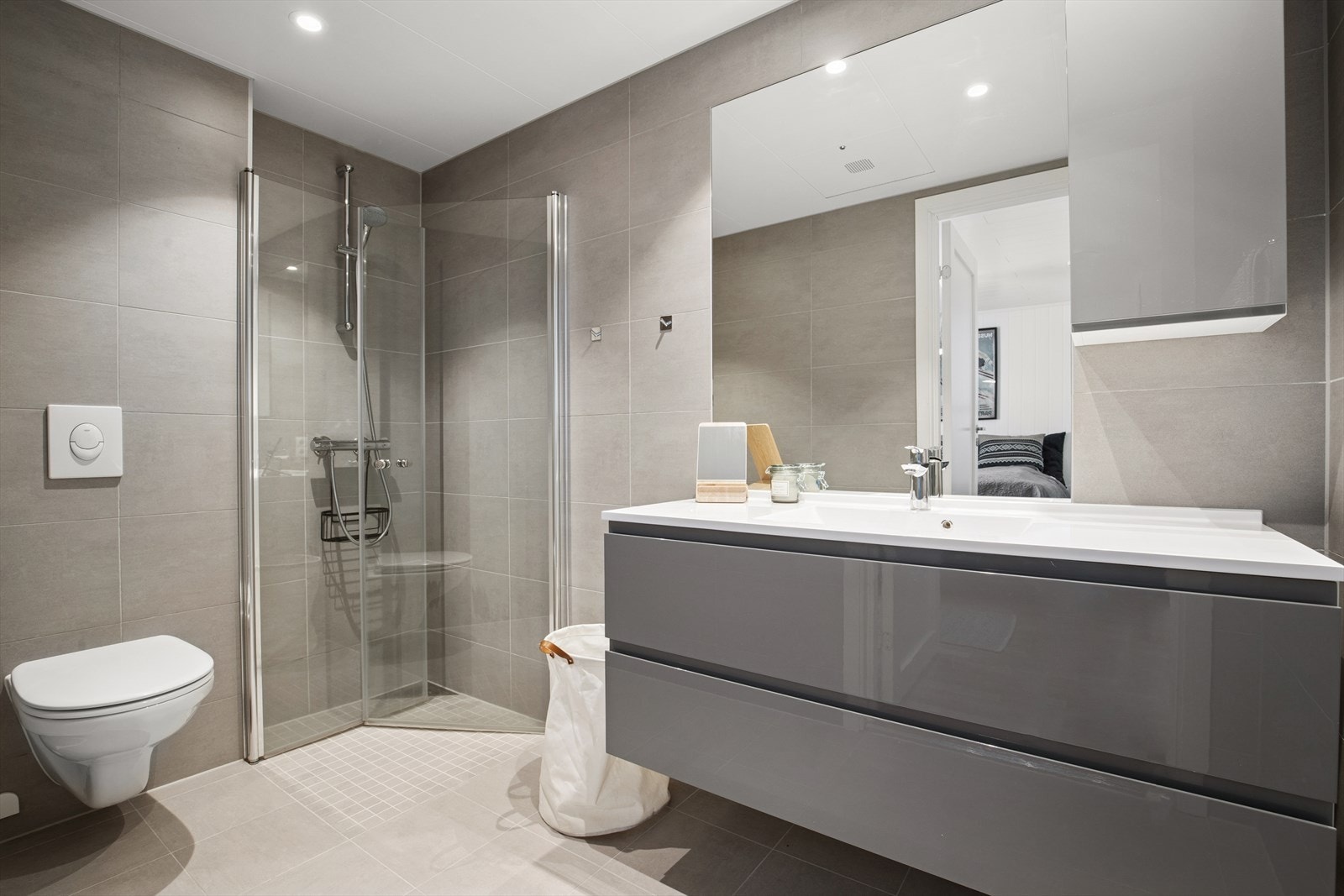 Flislagt bad i 1. etasjen med varmekabler, utstyrt med vegghengt toalett, dusjhjørne med glassdører, samt baderomsinnredning med heldekkende servant og speilskap. Galleribilde