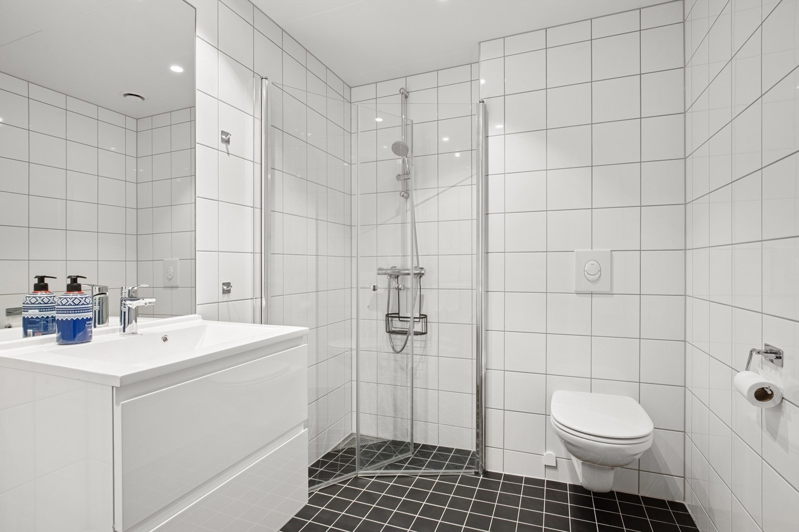 Flislagt bad i 2. etasjen med varmekabler, utstyrt med vegghengt toalett, dusjhjørne med glassdører, samt baderomsinnredning med heldekkende servant. Galleribilde