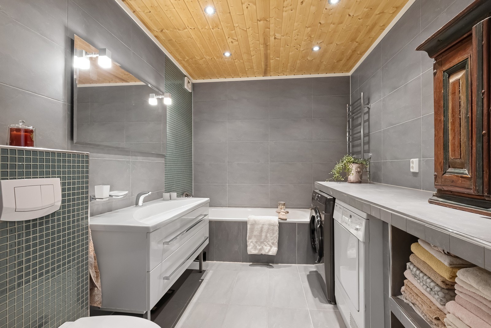 Flislagt baderom i 1. etasje med varmekabler i gulvet og downlights i himling. Badet er innredet med nedfelt servant på underskap med speil og belysning, vegghengt toalett og badekar. I tillegg er det opplegg for vaskemaskin og tørketrommel. Galleribilde