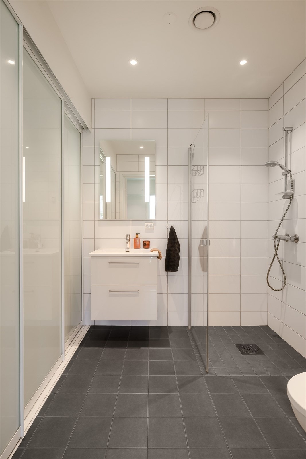 Badet har veggmontert toalett og baderomsinnredning med skuffer og heldekkende servant. I overkant av servanten er det speil med lys. Elektrisk uttak på vegg. Galleribilde