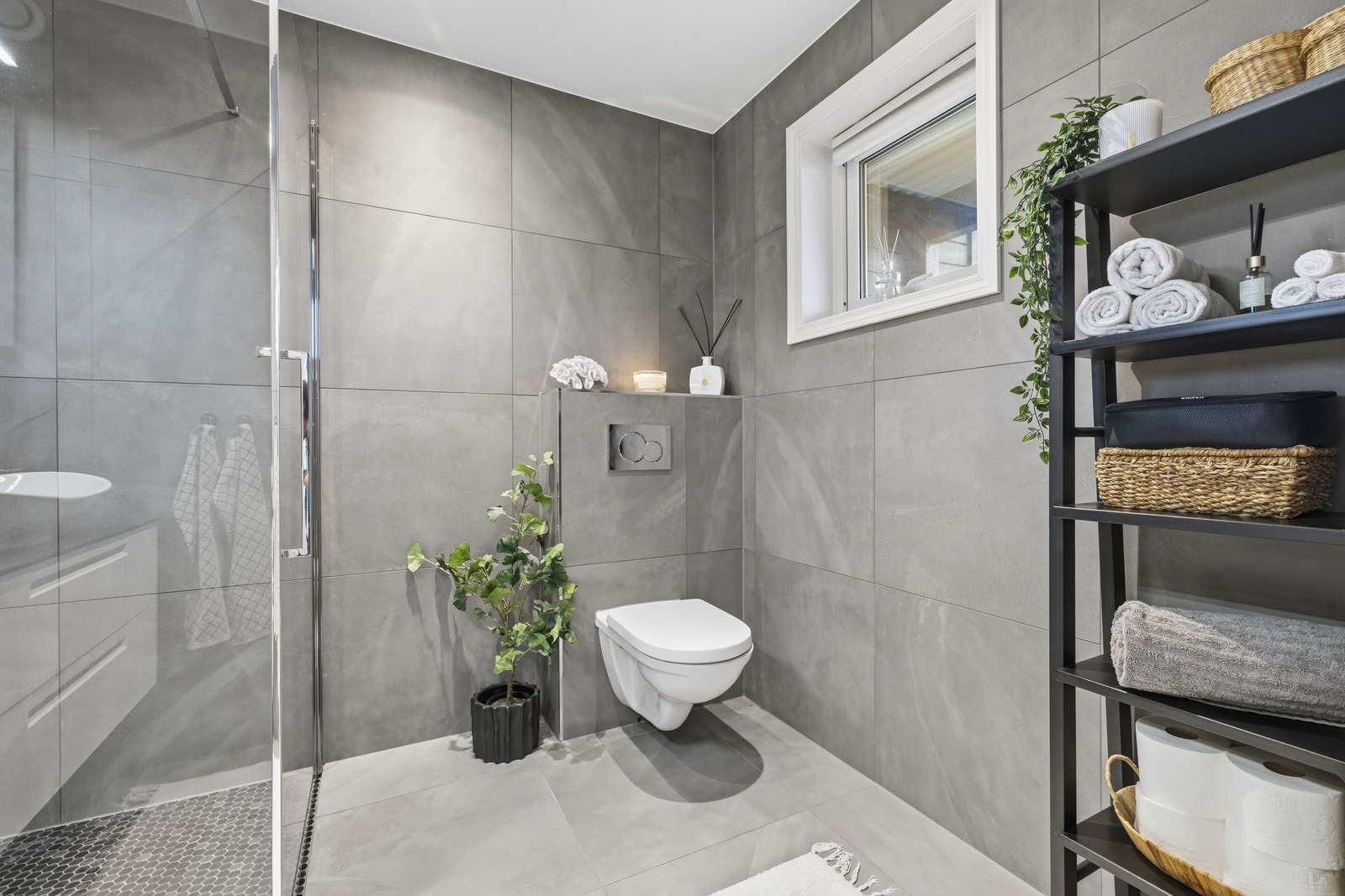 Badet har dusjnisje med glassdør, regnfallsdusj og dusjarmatur. Videre er det vegghengt servantskap med ovenpåliggende servant og ett-greps armatur, overskap med speildører, overlys på vegg over servant, samt innebygget sisterne med vegghengt toalett Galleribilde