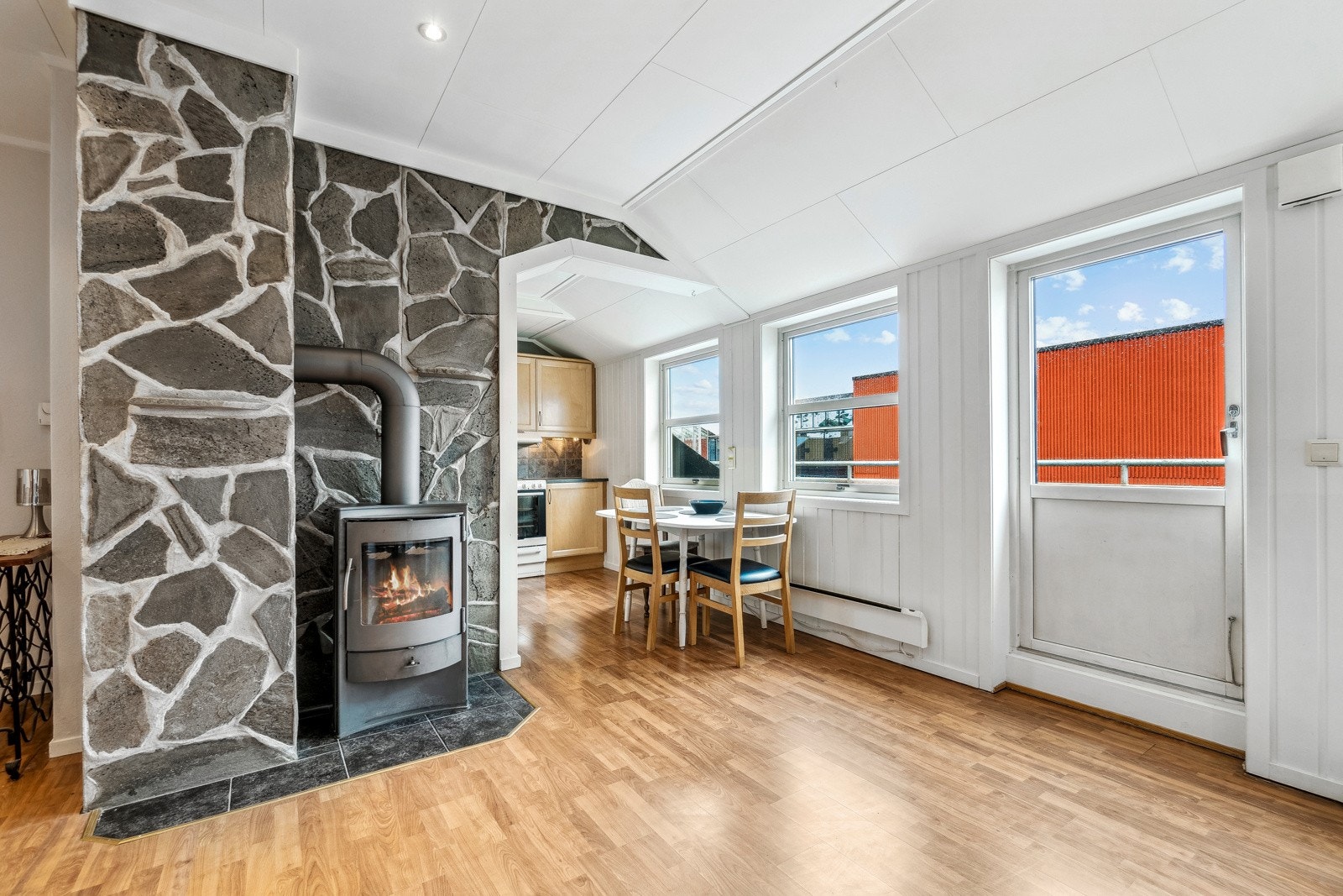 Lysinntaket fra vinduene sørger for at stuen holder seg lys og behagelig gjennom dagen, og vedovnen bidrar til en varm og god atmosfære på kjølige dager. Galleribilde