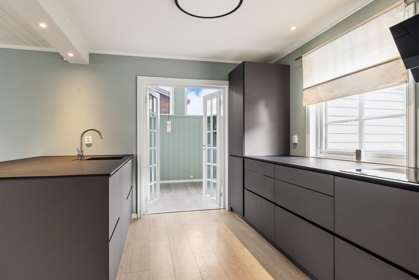 Moderne kjøkken med slette, mørke fronter og god benkeplass. Fra kjøkkenet er det utgang til en innglasset hagestue. Galleribilde