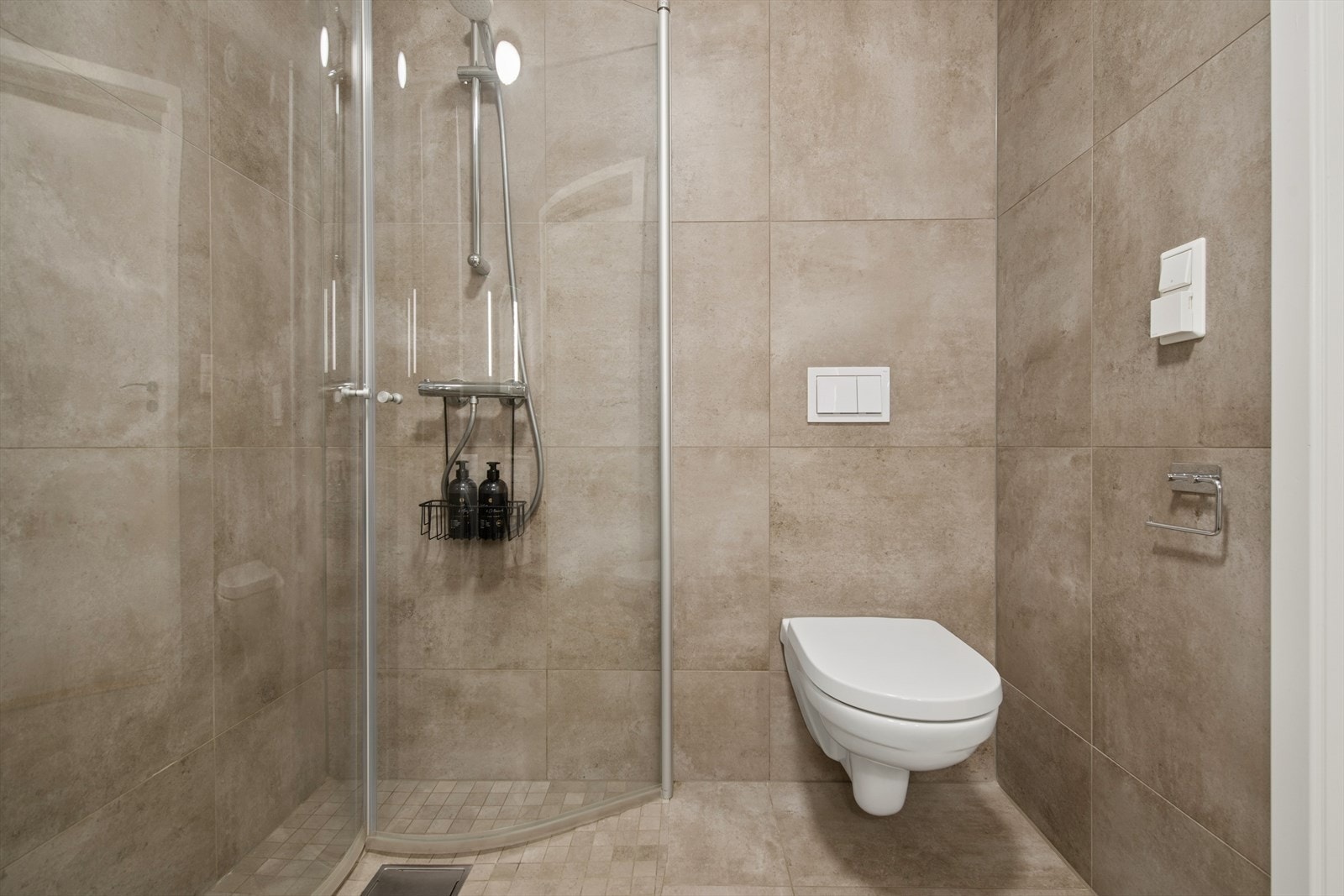 Badet er helfliset og utstyrt med vegghengt toalett og dusjhjørne med innfellbare glassdører. Galleribilde