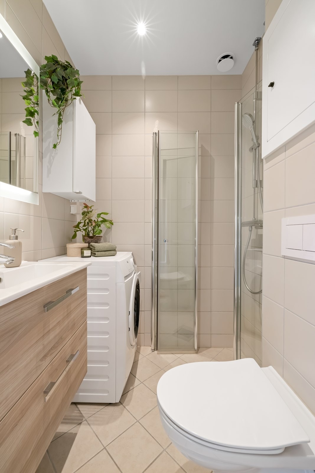 Badet er innredet med veggmontert toalett, dusj med glassvegger, servantinnredning og opplegg for vaskemaskin. Det er naturlig ventilasjon. Galleribilde