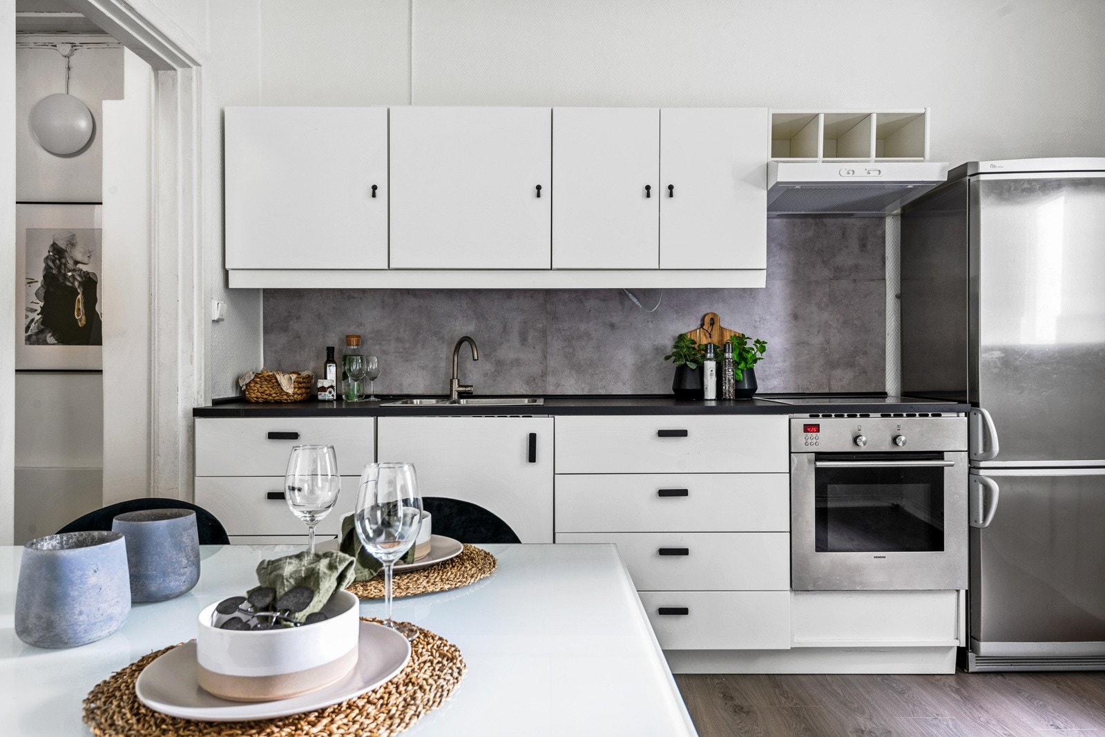 Lys kjøkkeninnredning med hvite glatte fronter og laminert benkeplate med nedfelt oppvaskkum. Praktisk med plater i benkeryggen og belysning under overskap. Galleribilde