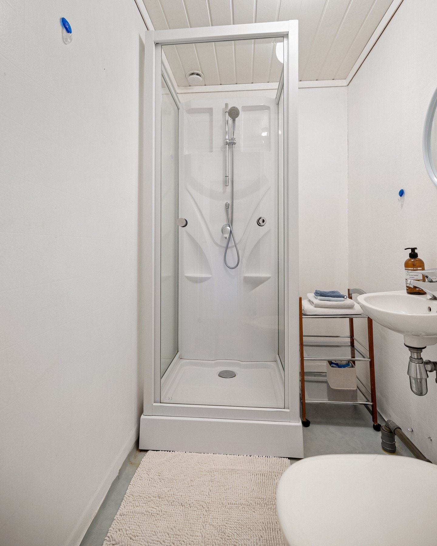 Badet er utstyrt med dusjkabinett, servant og toalett. Rommet har tilsvarende enkle overflater med vegger i plater/tapet og belegg på gulv. Standard og utførelse bærer preg av alder, og løsningene er i hovedsak fra byggeår. Galleribilde