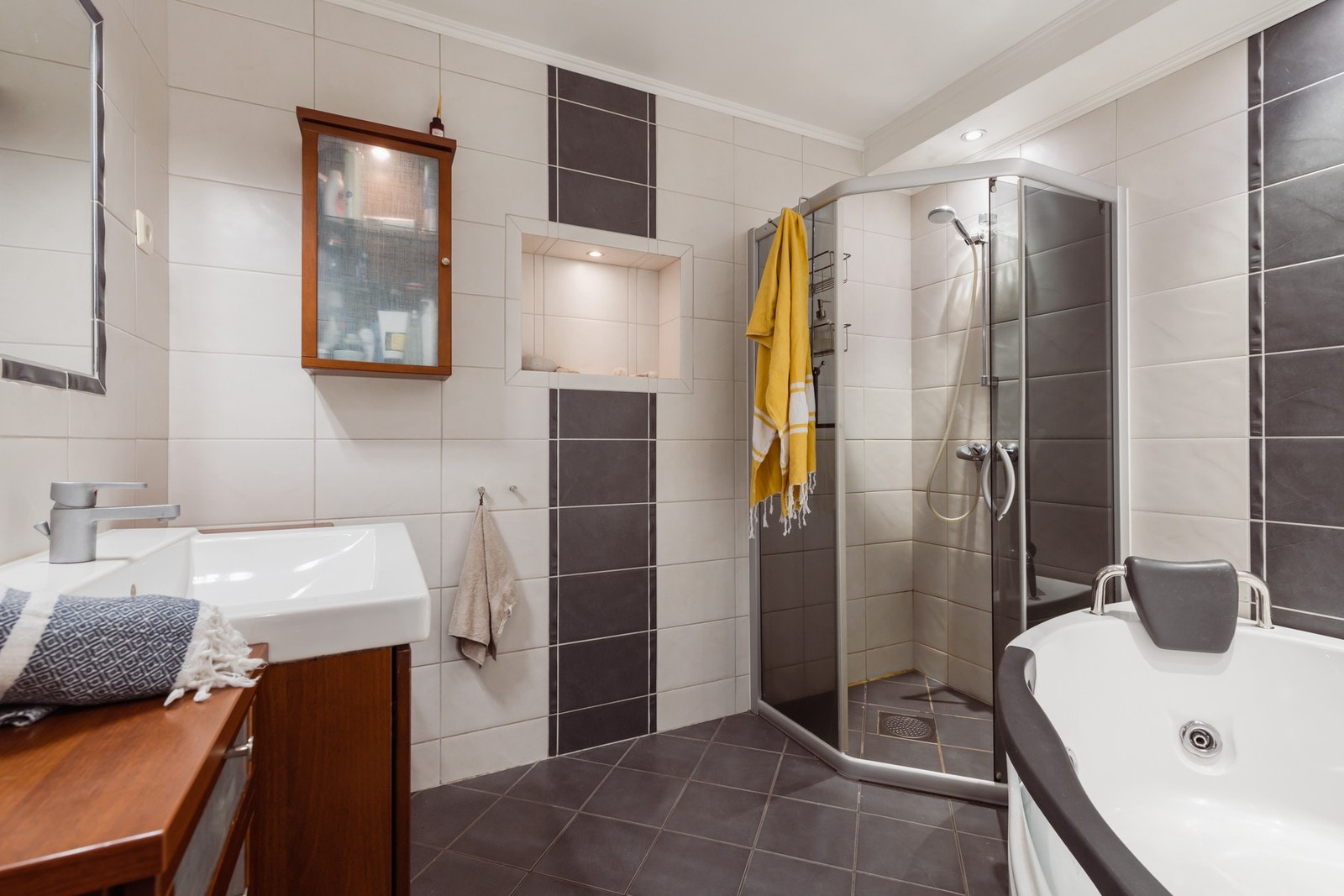 Badet har downlights i himlingen, hvite og koksgrå fliser på veggene og matchende fliser på gulv med gulvvarme. Galleribilde
