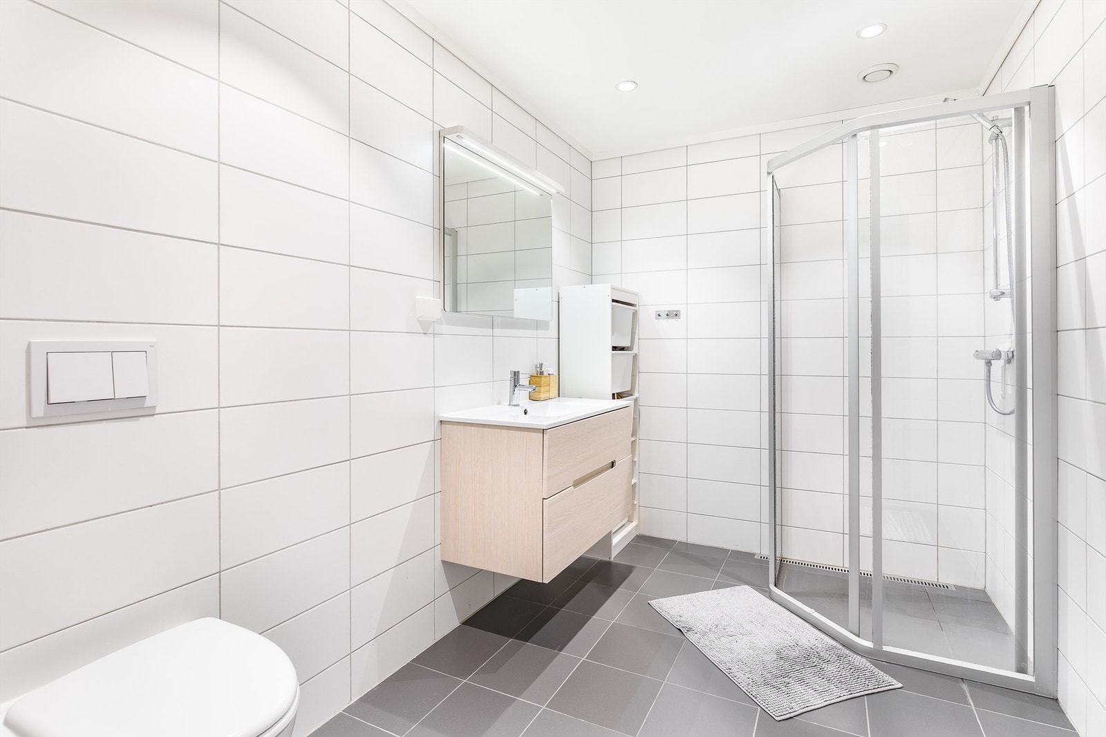 På badet er gulvet og veggene utført med fliser, himlingen med innfelte LED-spotter som kan dimmes. Galleribilde