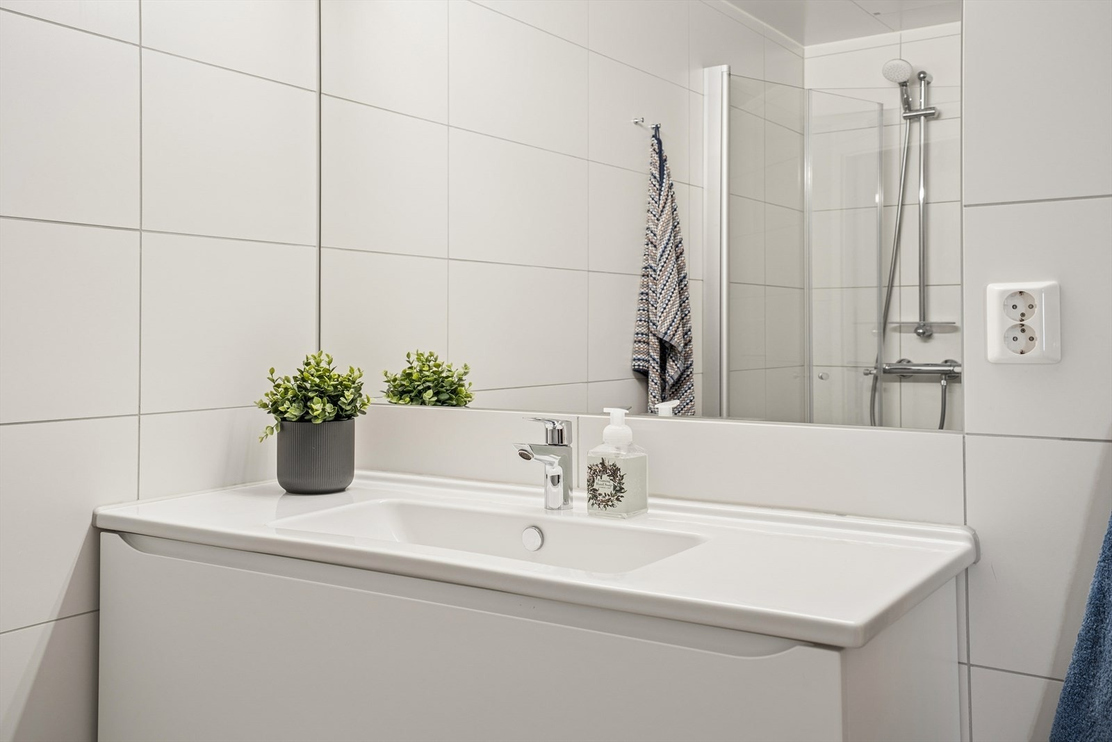 Badet er innredet med vegghengt toalett, servant og åpen dusjsone med dusjgarnityr på vegg Galleribilde