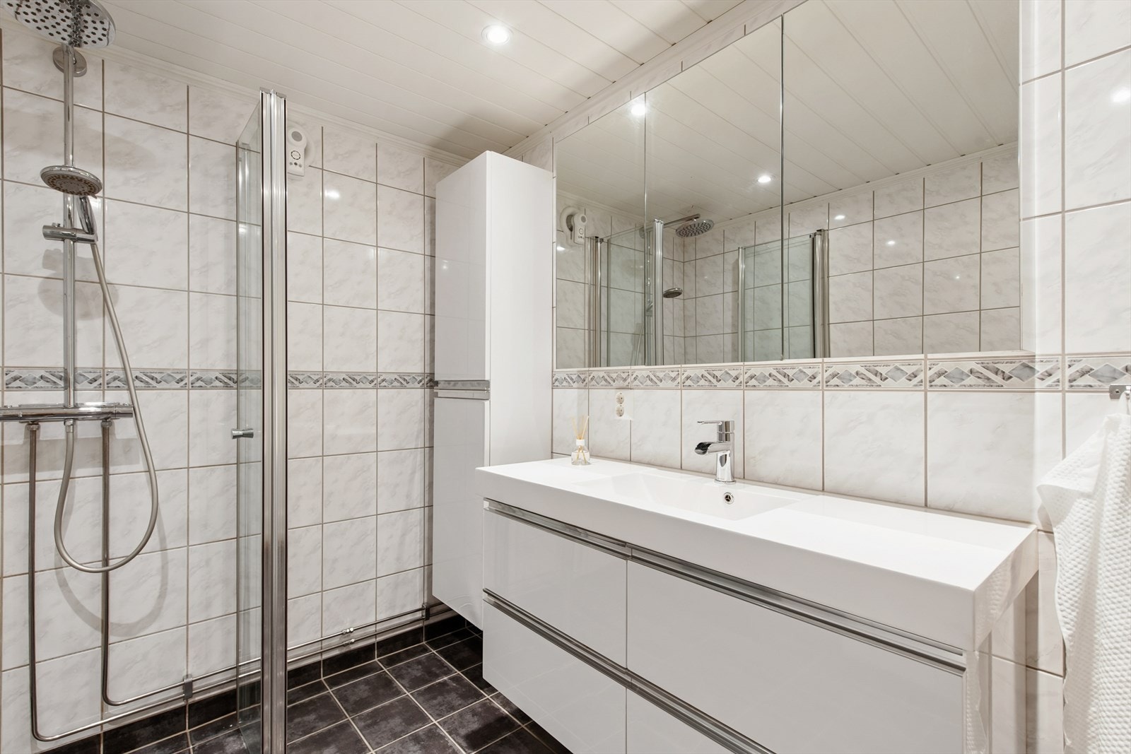 Badet har fliser på gulv og vegger, lys innredning og speilskap Galleribilde