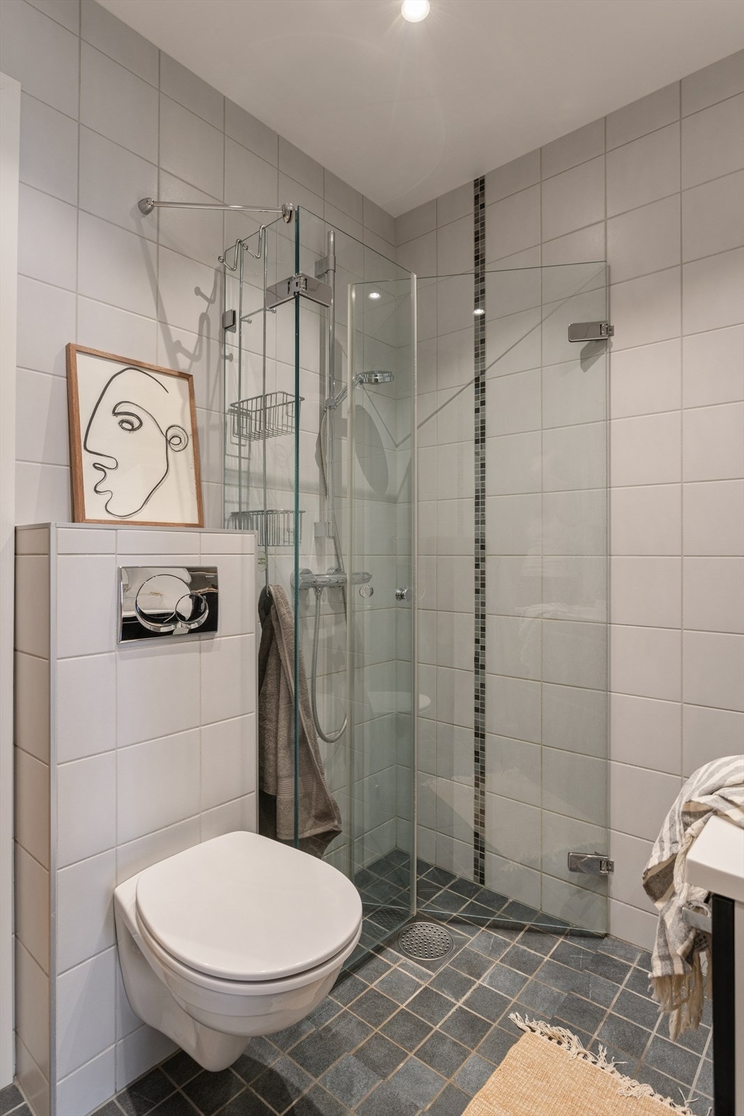 Det er downlights i himling og varmekabler på gulv. Innredning består av servant med skuffeseksjon, speil med lys, veggskap, vegghengt klosett og dusjhjørne med svingbare glassdører. Galleribilde