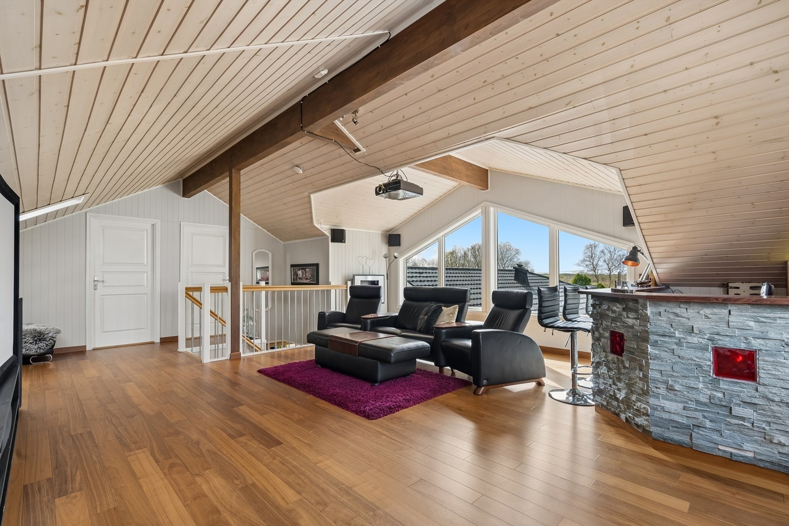 Loftstuen tilbyr et romslig oppholdsrom med lysinnslipp fra store vinduer og god takhøyde. Her er det i dag hjemmekino og bar. Galleribilde