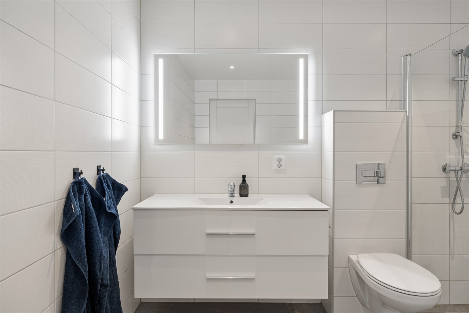 Moderne baderomsinnredning med heldekkende servant og speil med integrert belysning. Galleribilde