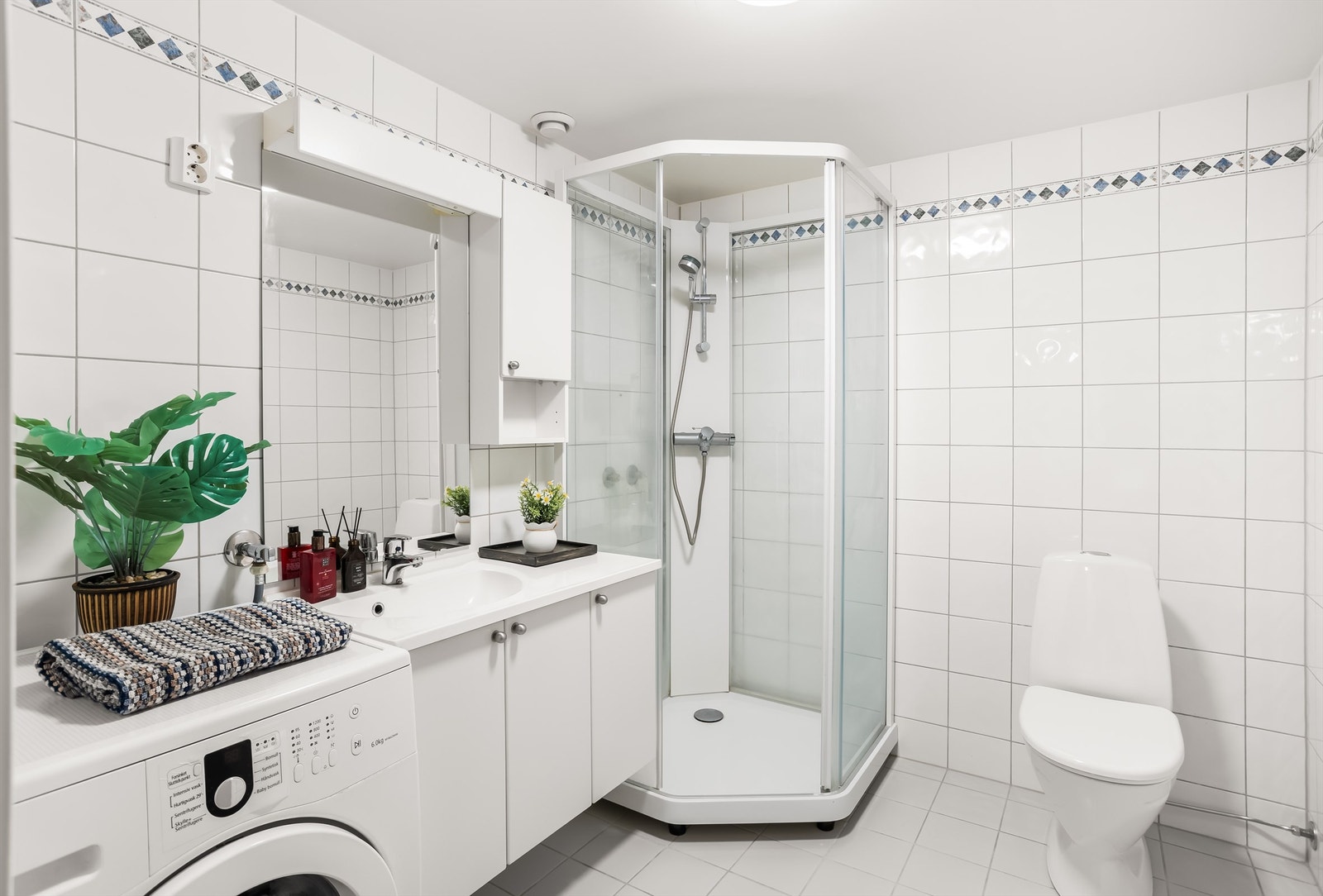 Flislagt bad med gulvvarme, dusjkabinett, servantinnredning, toalett og opplegg for vaskemaskin. Galleribilde