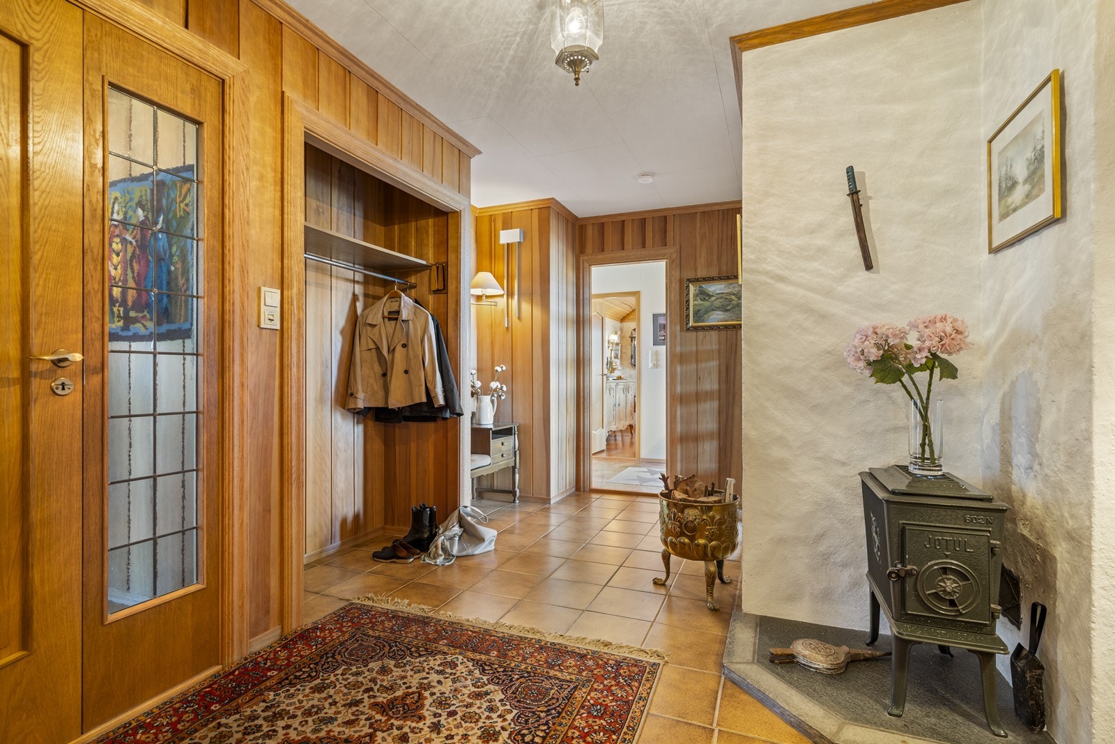 Romslig og innholdsrik gang med parana pine på vegg og flislagt gulv. Eikedører med eikelister. Galleribilde