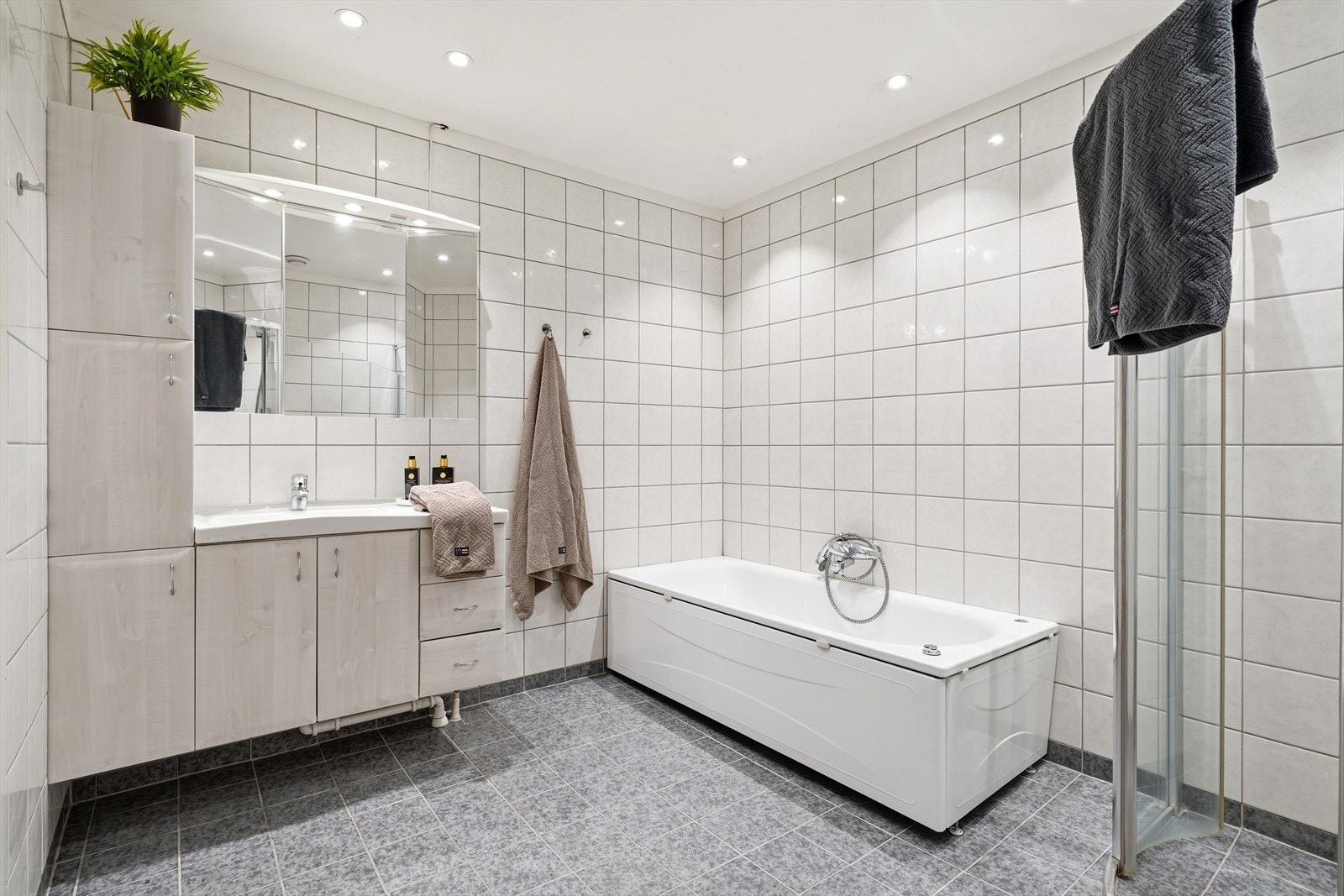 Baderom innredet med servant m/skuffer og skap, toalett, badekar og dusjvegger/hjørne. Galleribilde