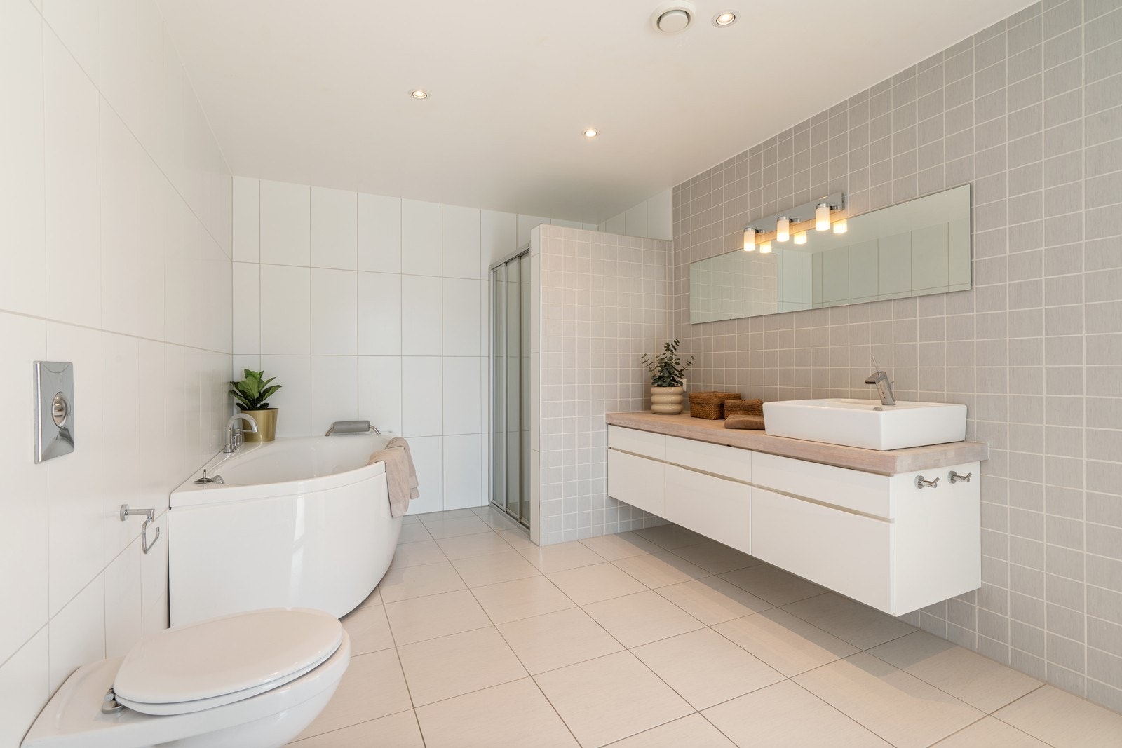 Badet er stilrent innredet med servant på baderomsmøbel, vegghengt toalett samt både badekar og dusjløsning med vegger/hjørne Galleribilde