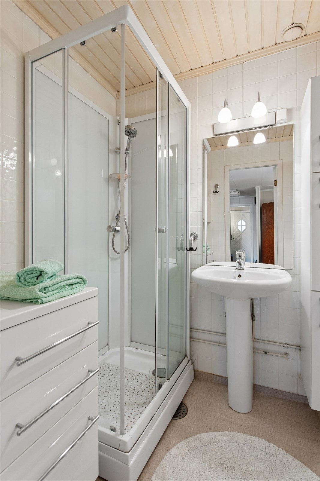 Badet er utstyrt med dusjkabinett og servant. Rommet har våtromsbelegg på gulv og vegger fra 1990. Galleribilde