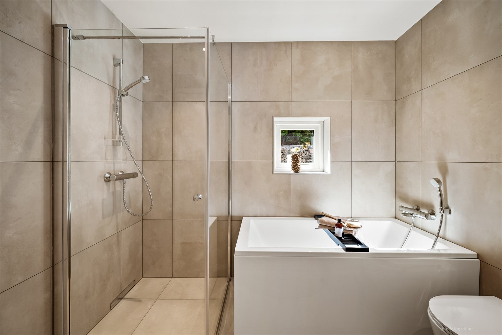 Badet i første etasje er innredet med badekar, dusjhjørne, vegghengt toalett og hvit baderomsinnredning med speilskap. Galleribilde