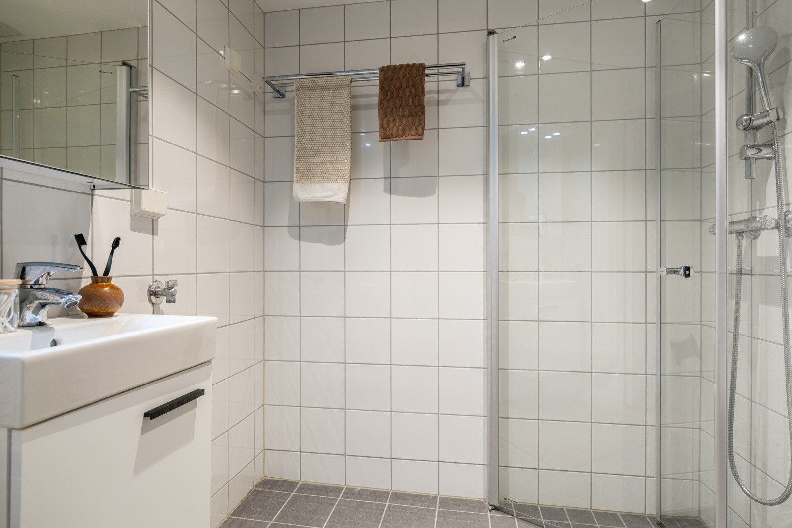 Leiligheten har et lyst og moderne baderom fra 2015. Baderommet har grå fliser på gulv, elektriske varmekabler, lyse fliser på veggene og mekanisk avtrekk. Galleribilde