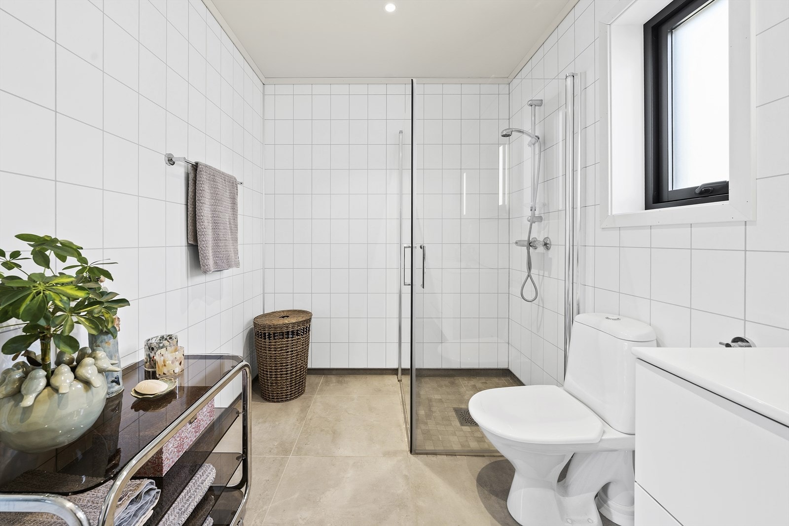 Badet er utstyrt med heldekkende servant over skuffeinnredning, speil med belysning, dusjhjørne med innfellbare glassvegger og toalett Galleribilde
