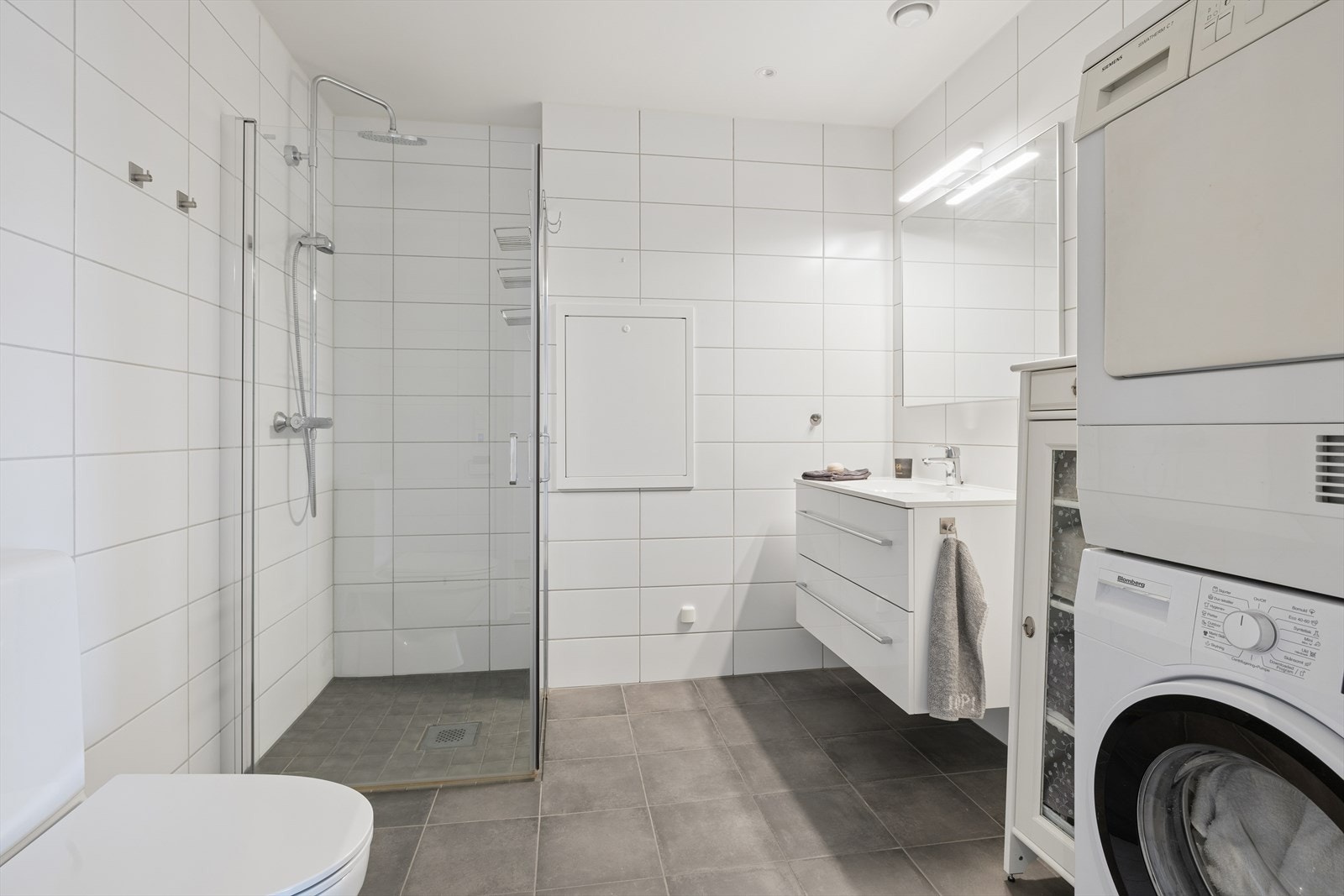 Badet er helfliset og utstyrt med dusjhjørne med innfellbare glassdører, vegghengt toalett og servantinnredning. Galleribilde